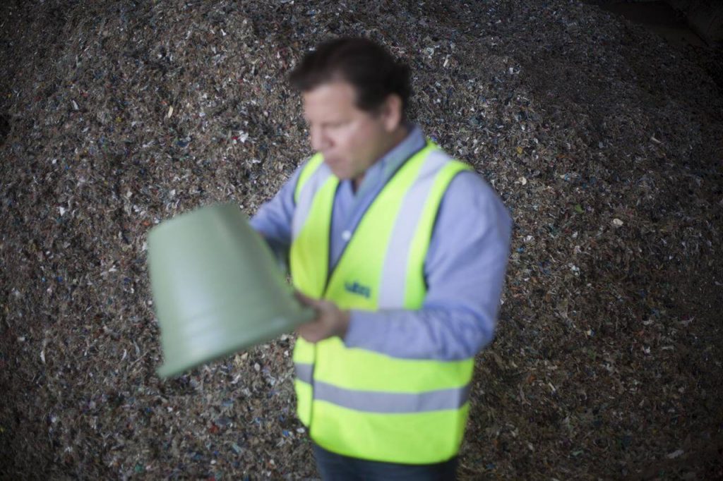 Jack Tato Bigio co-Founder and Chief Executive at UBQ, holds a recycled plastic bucket next to a pile of dried and shredded garbage