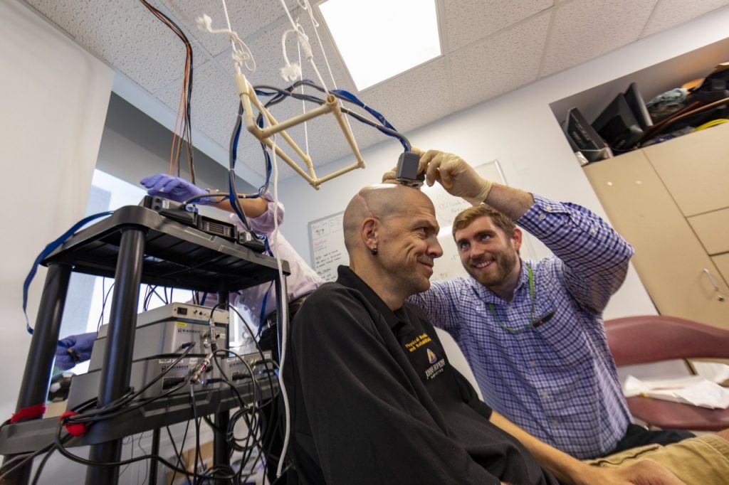 Matt Fifer adjusts the electrodes attached to Buz Chmielewski's head to prepare for a round of testing. The image is adapted from the Johns Hopkins University news release