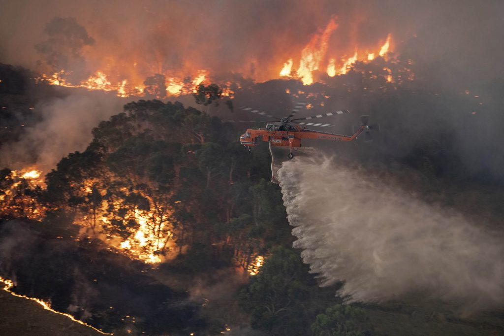 In this Monday, Dec. 30, 2019 photo provided by State Government of Victoria, a helicopter tackles a wildfire in East Gippsland, Victoria state, Australia. Wildfires burning across Australia's two most-populous states trapped residents of a seaside town in apocalyptic conditions Tuesday, Dec. 31, and were feared to have destroyed many properties and caused fatalities