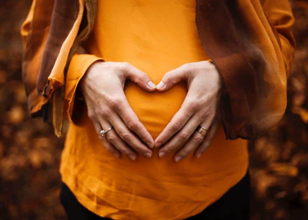 pregnant woman holding hands on stomach in shape of heart
