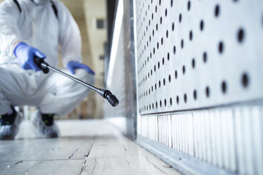 A technician in a protective suit performing pest control in a home.