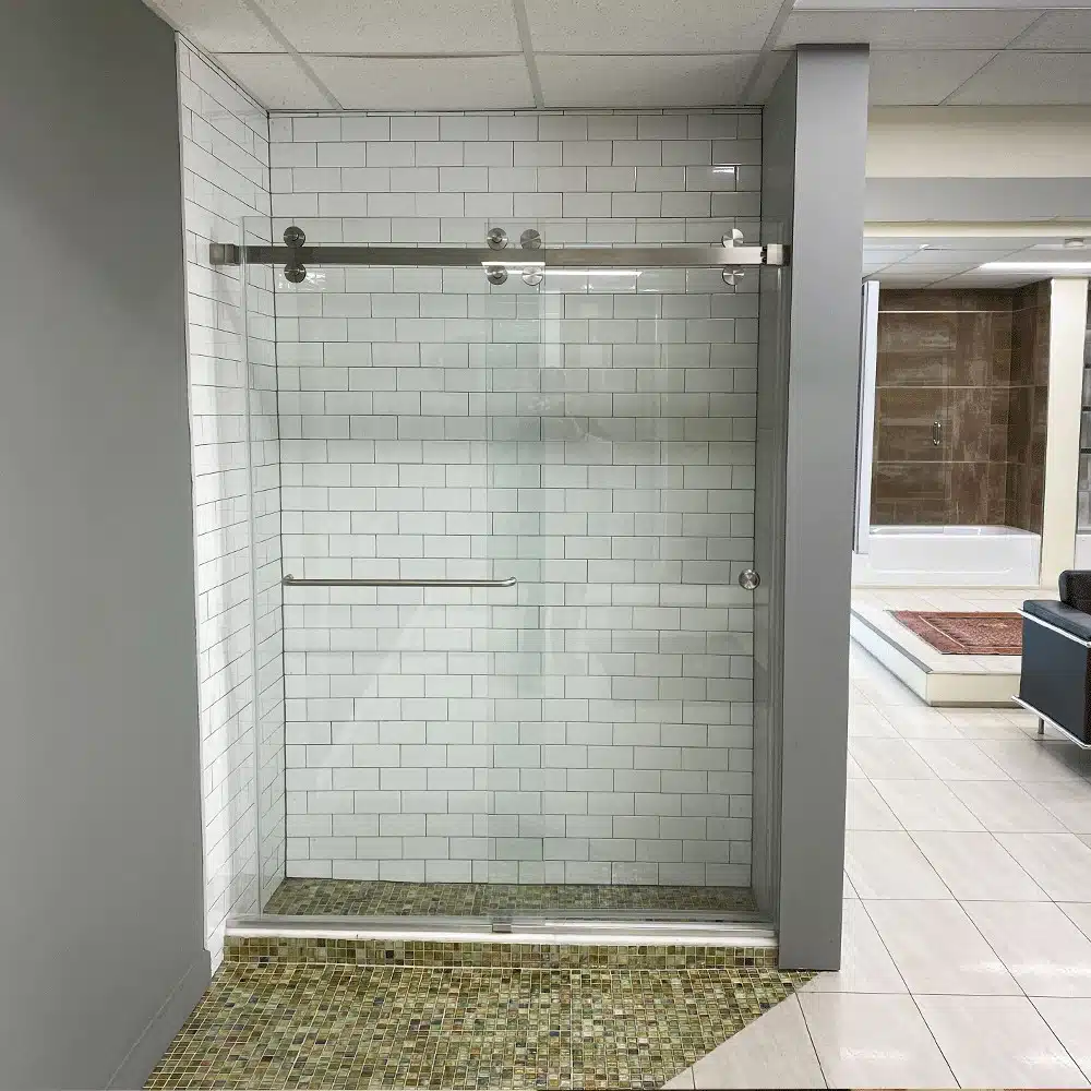 A modern glass shower door with white subway tile and a mosaic tile floor.