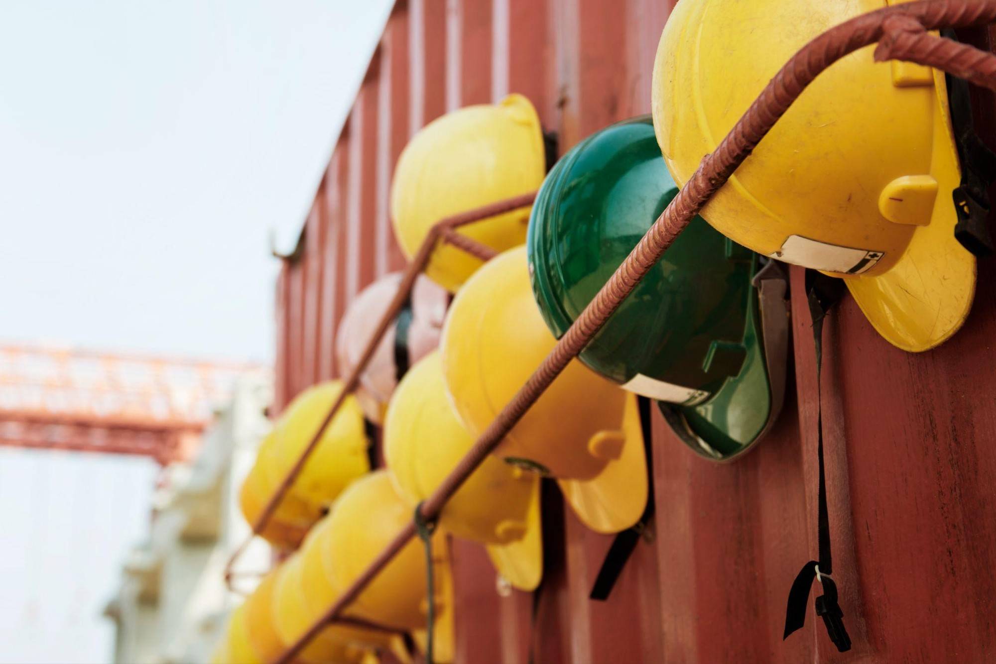The Building Materials Still Sitting in Millions of Homes Several yellow and one green hard hat are hanging on a metal bar in front of a red corrugated wall.