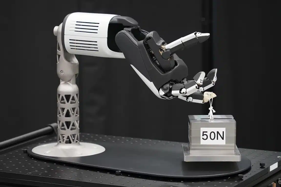 A robotic hand delicately holding a small object attached to a string, positioned above a cube with '50N' labeled on its side.