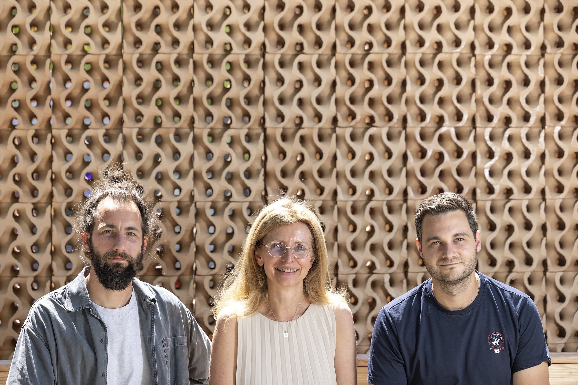 Three people, two men and one woman, posing in front of a textured wall.
