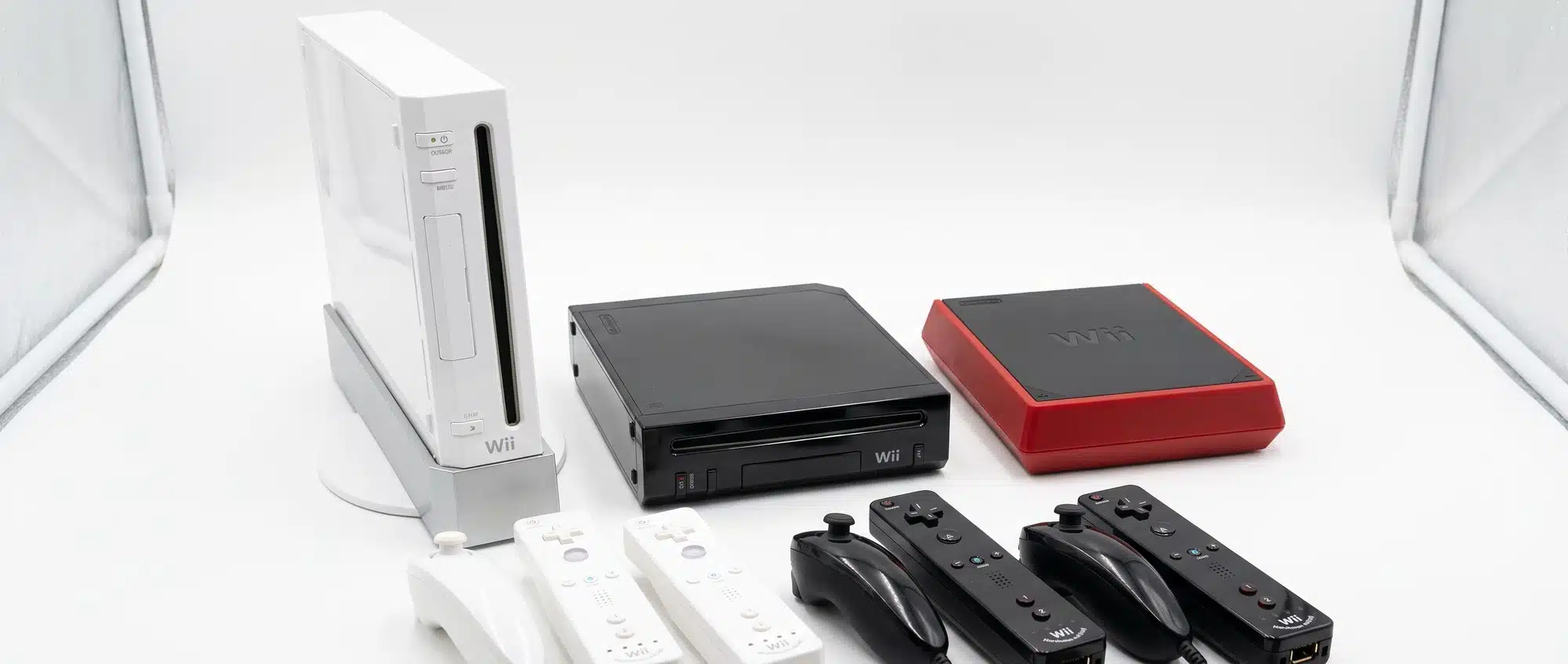 All three Nintendo Wii models side by side with white original black family edition and red Wii Mini