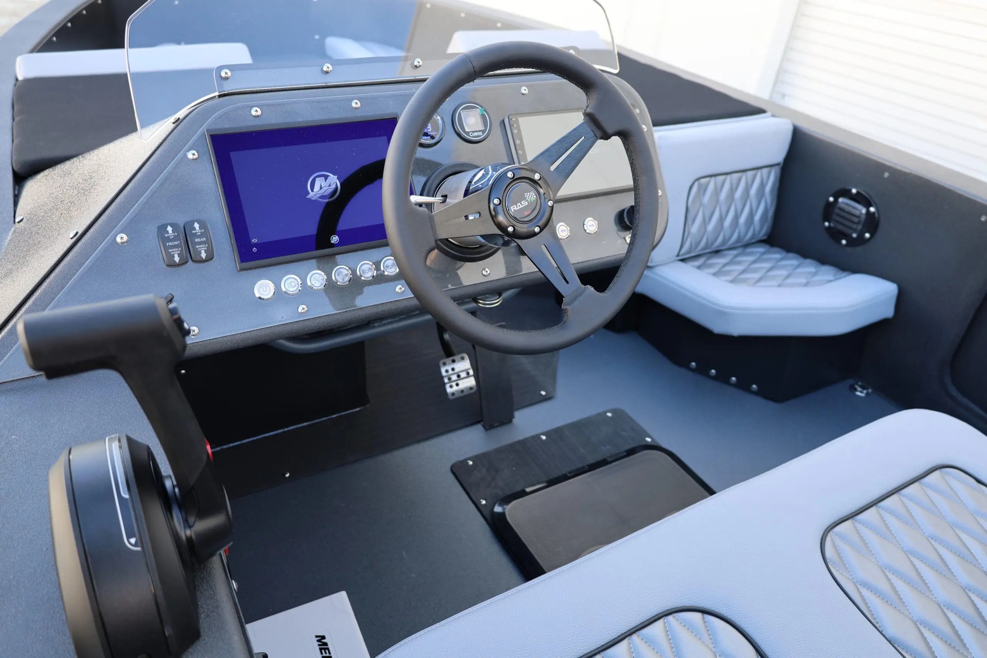 The helm of a WaterCar amphibious vehicle, showing its dual-screen dashboard, steering wheel, throttle, and quilted grey and black seating.