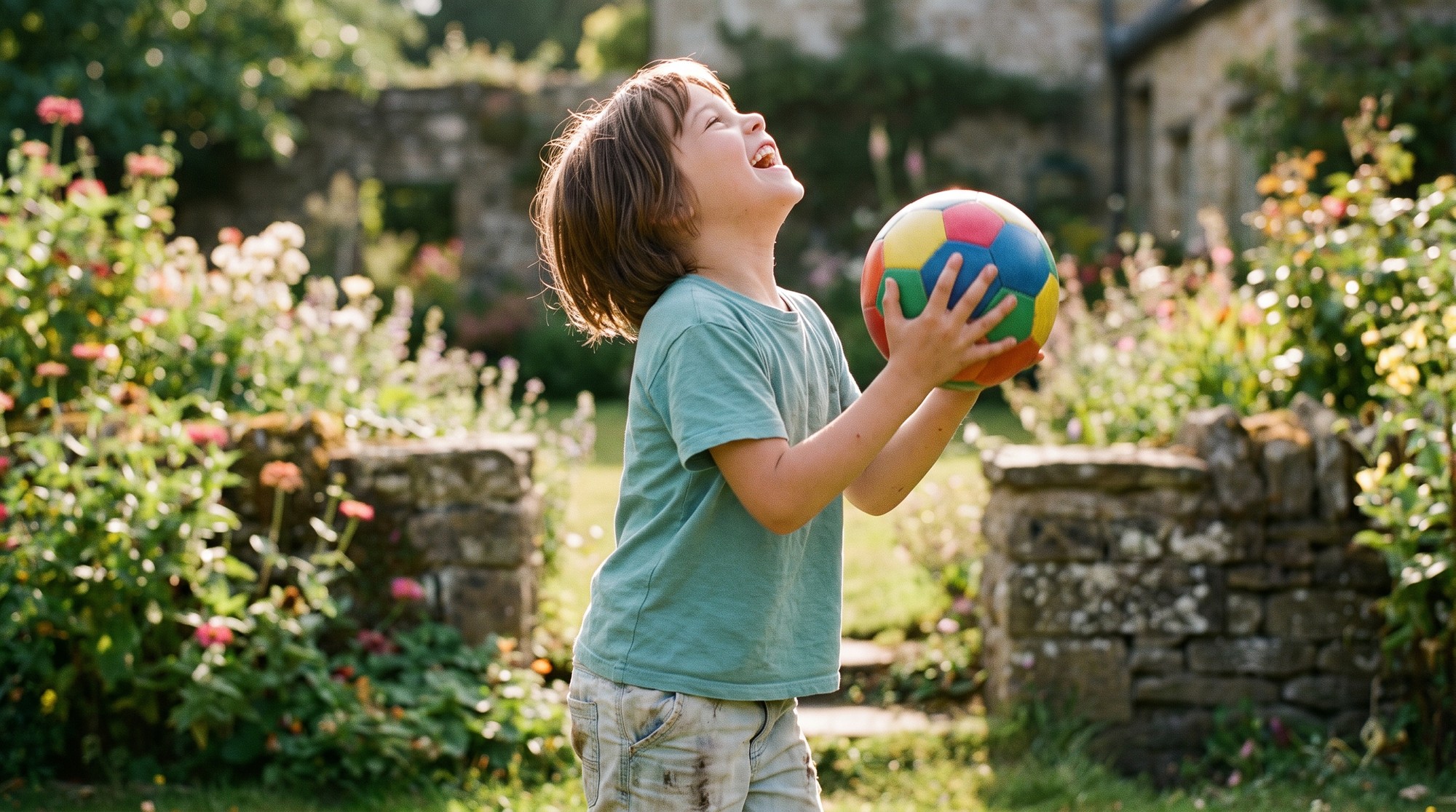 A cheerful young child with short natural-looking hair laughing while playing with a ball in a sunny garden.