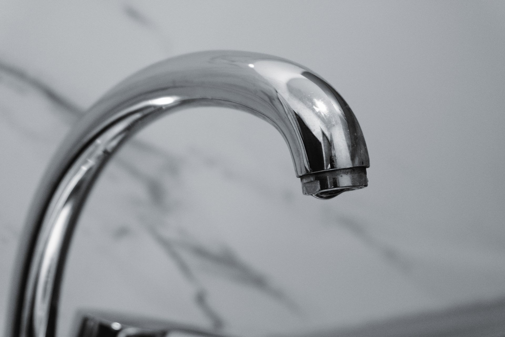What to Do When Water Damage Starts Quietly Taking Over Your Home A close-up of a modern chrome water faucet with a single water droplet hanging from the tip against a marble background.