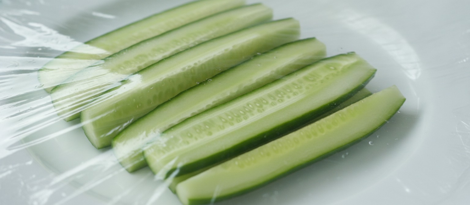 Close-up of clear biodegradable food wrap film stretching over fresh cucumber slices