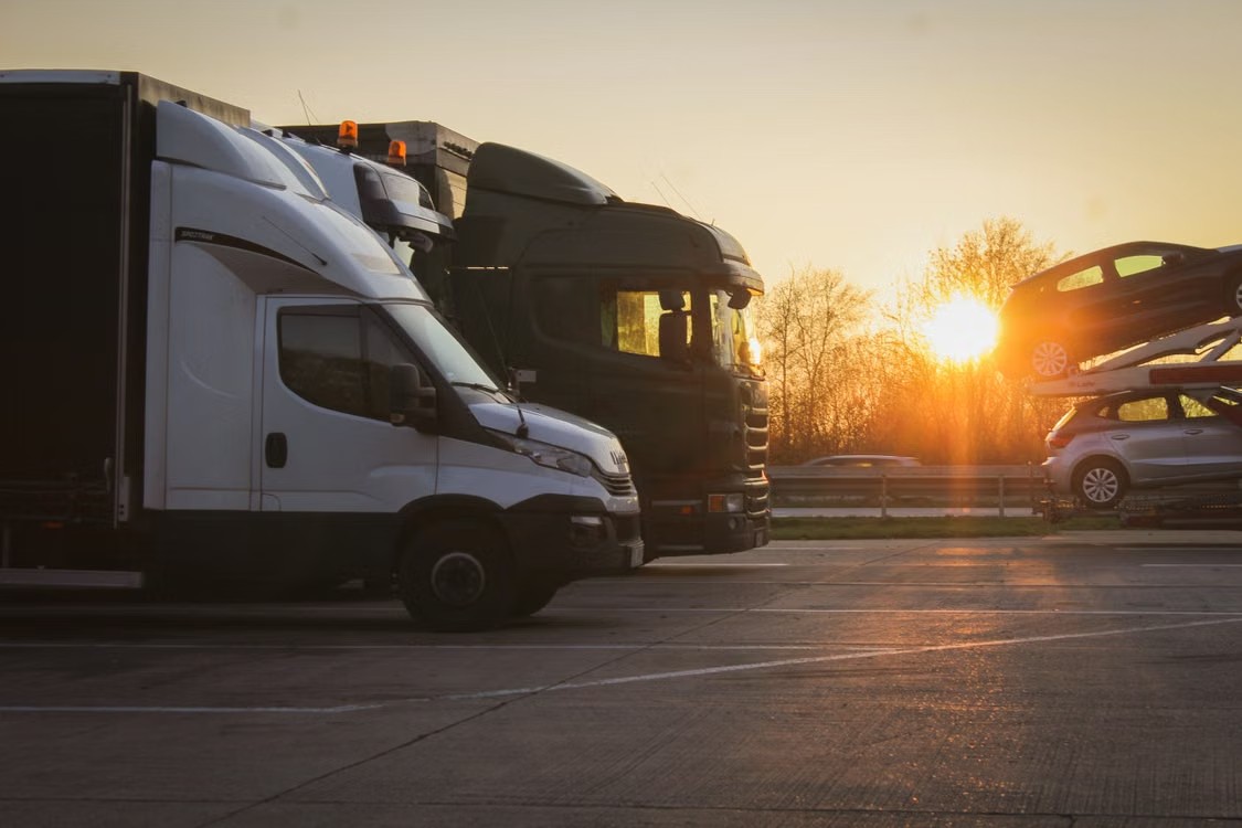 Federal Safety Mandates Are Reshaping Operational Standards Across Transportation Commercial transport trucks parked in a lot during sunset, with a car carrier visible in the background.