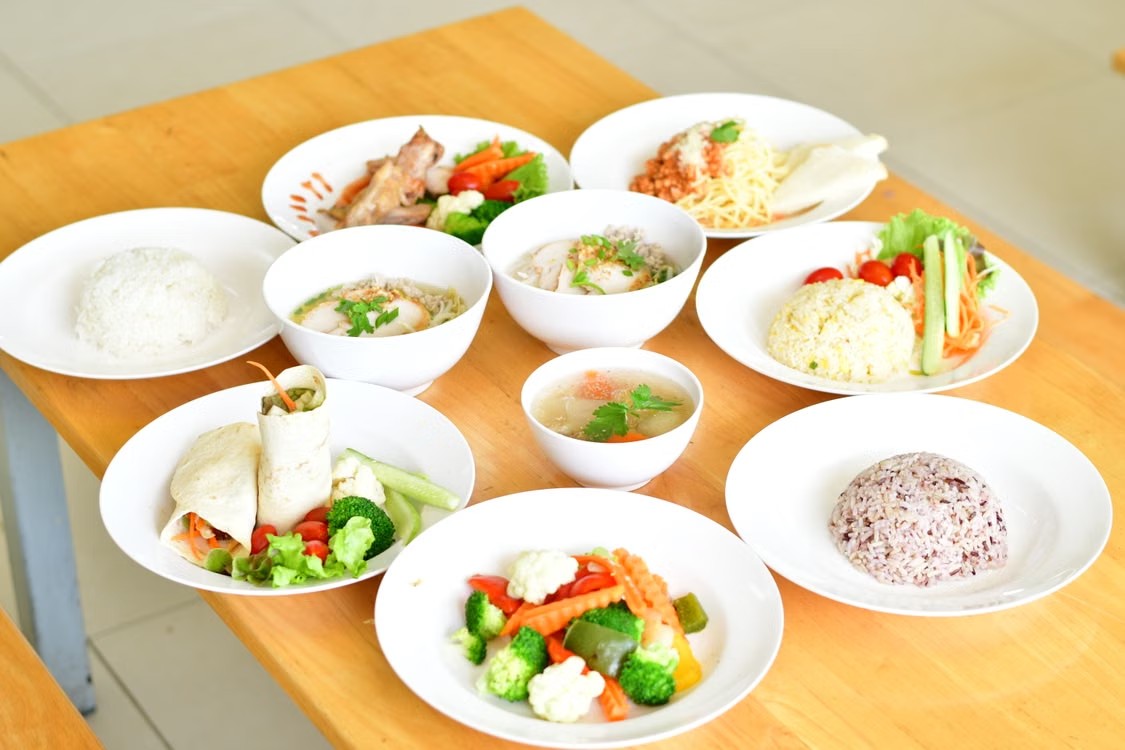A wooden table displaying various healthy meals, including rice dishes, soups, wraps, and vegetables for industrial crew nutrition.