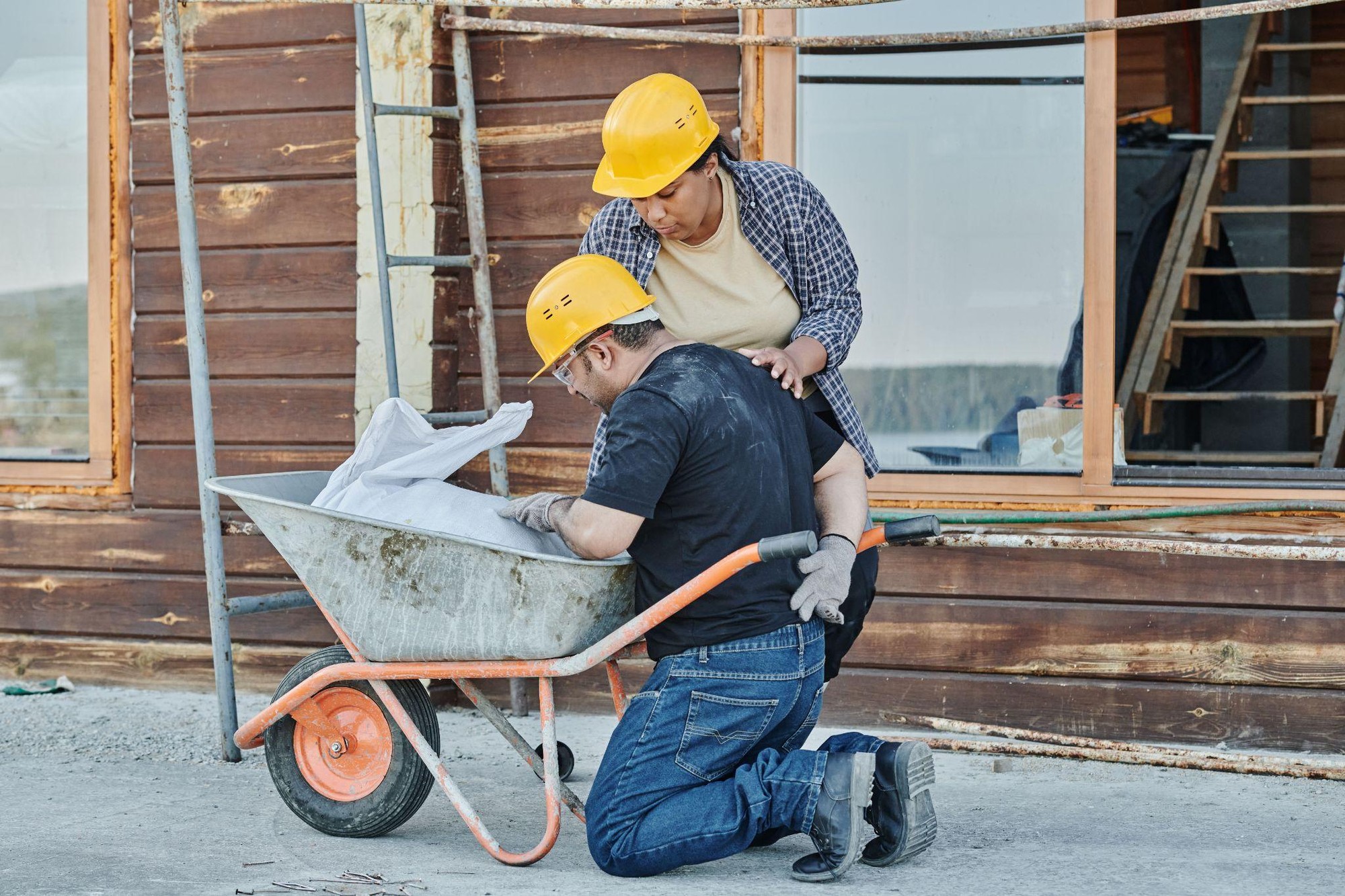 Healing After a Workplace Injury: What to Expect A construction worker kneeling in pain by a wheelbarrow while a colleague checks on him.