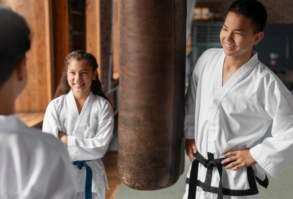 How Karate Clubs Can Better Prepare for Liability and Everyday Risks Four martial arts students in white uniforms and coloured belts standing in formation on a padded dojo mat.