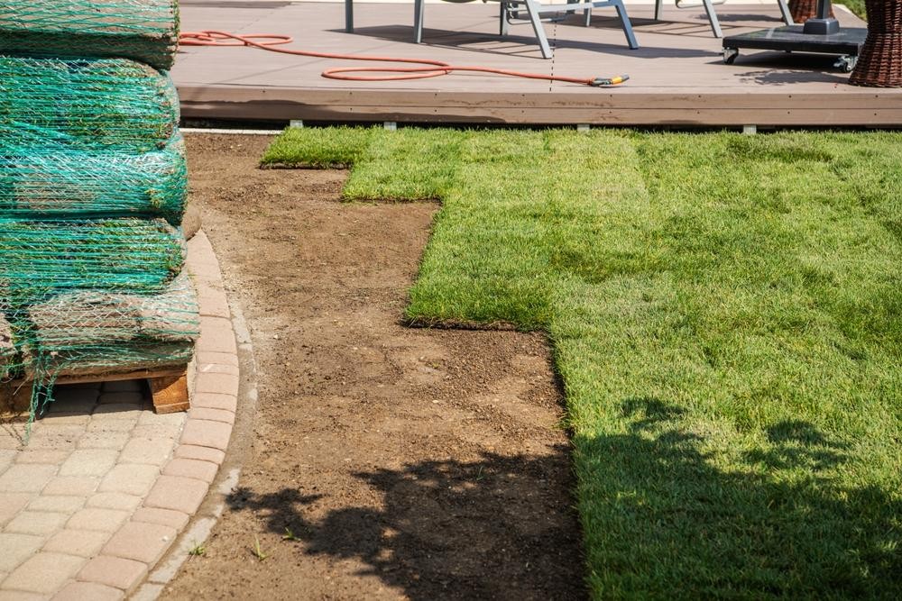 Freshly laid sod rolls and patches of grass being installed in a backyard next to a wooden deck.