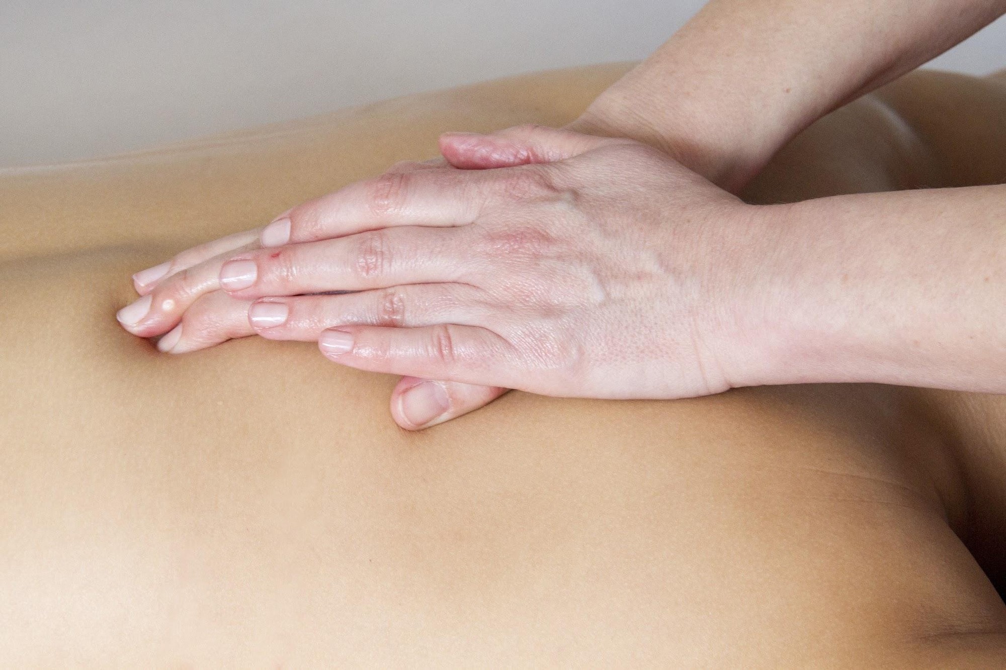 A physical therapist's hands performing soft tissue massage and mobilization on a patient's back.