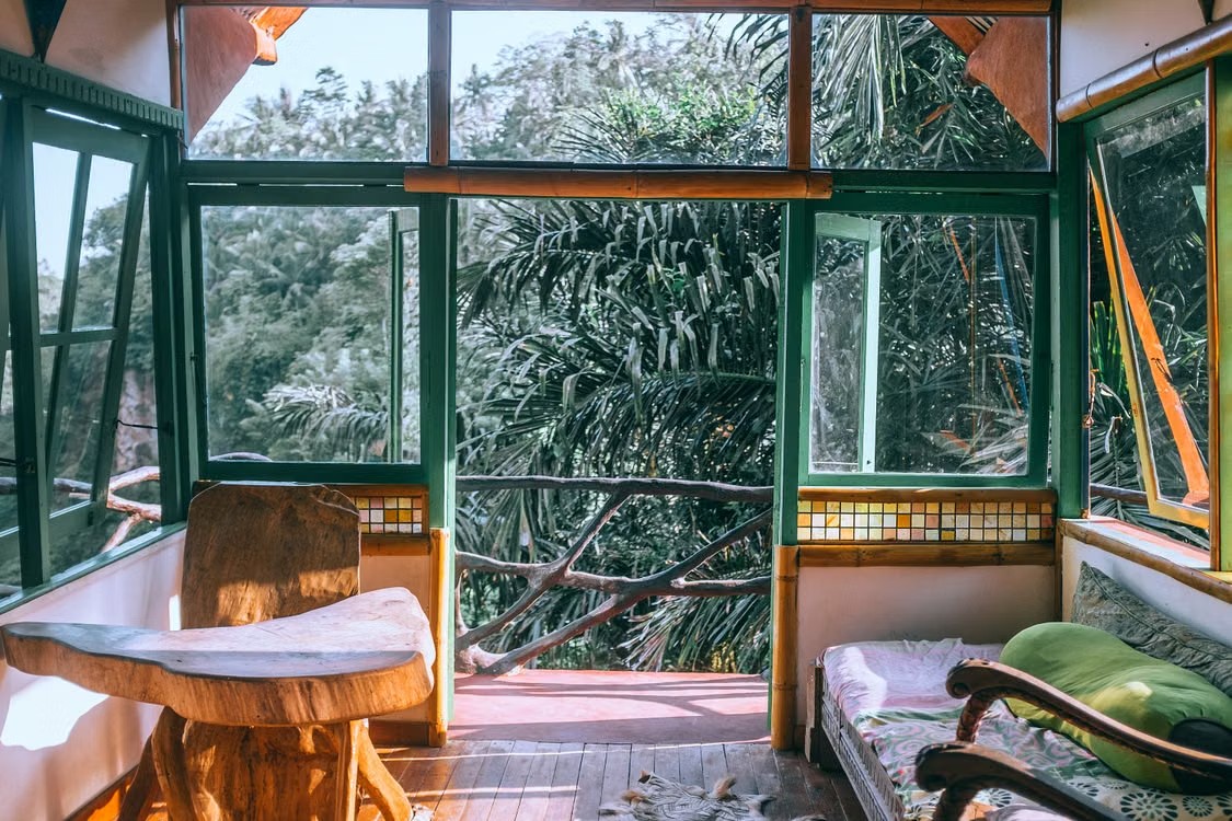 A bright living space filled with wooden furniture and large windows overlooking lush green trees.