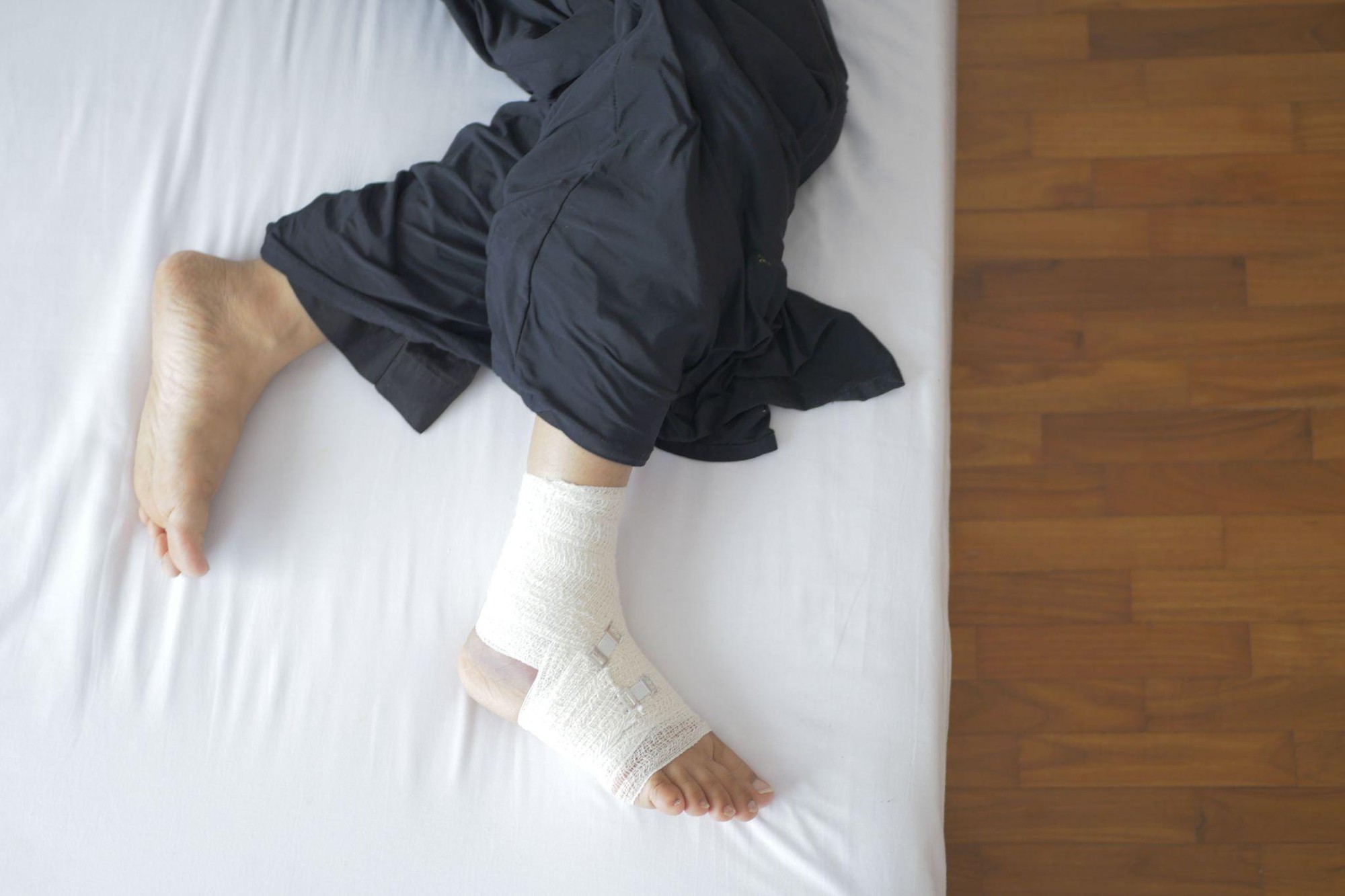 A person resting on a bed with an elastic bandage wrapped securely around their injured foot and ankle.