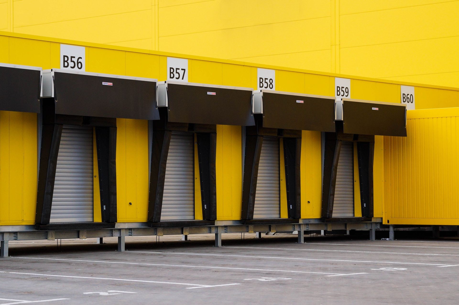 A row of yellow loading docks with numbered signs B56, B57, B58, B59, and B60.